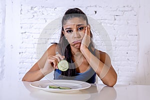 Depressed dieting woman holding folk looking at small green vegetable on empty plate