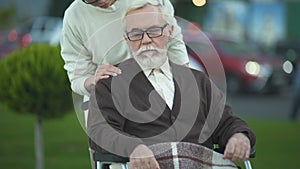 Depressed disabled elderly male in wheelchair stroking young female hand, family