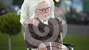 Depressed disabled elderly male in wheelchair stroking young female hand, family