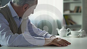 Depressed elderly man sitting at kitchen table, widower suffering loneliness