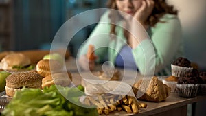 Depressed fat lady sitting at table full of unhealthy junk food, overeating