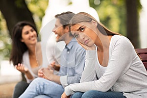 Depressed Girl Sitting Next To Happy Friends In Park Outside