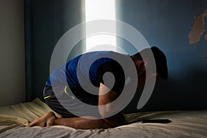 Depressed Hispanic man with hands covering his face while sitting inside a dark room