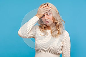 Depressed hopeless woman with curly blond hair making facepalm gesture, shame, getting into trouble, making mistake