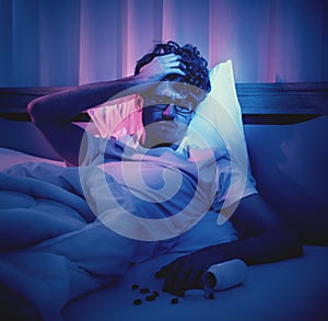 Depressed insomnia man holding his head on a bed late at night with Black Medical pills for stress and suicide concept