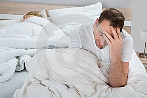 Depressed man on bed while woman sleeping