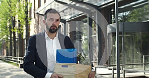 Depressed man carrying box with his stuff and looking downcast after loosing job. Dismissed male employee walking at