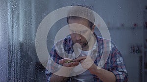 Depressed man counting coins behind rainy window, low incomes, poverty concept