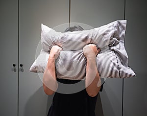 Depressed man covering his face with pillow and screaming in anger