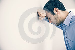 Depressed man leaning his head against a wall