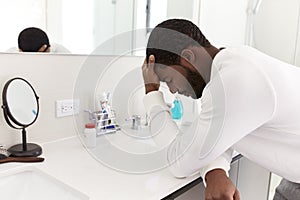 Depressed Man Leaning On Sink In Bathroom With Head In Hands