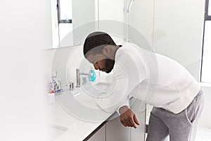 Depressed Man Leaning On Sink In Bathroom Looking Unhappy