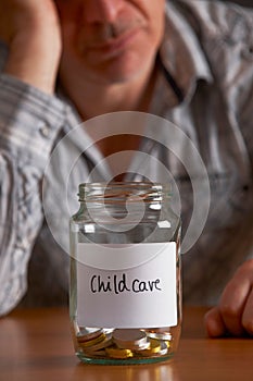 Depressed Man Looking At Empty Jar Labelled Childcare