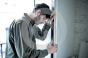 Depressed man looking out a window at home in mental health concept