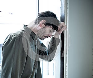 Depressed man looking out a window at home in mental health concept