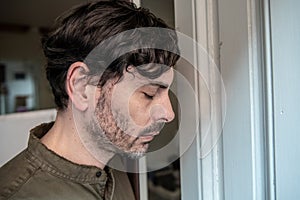 Depressed man looking out a window at home in mental health concept