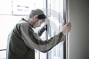 Depressed man looking out a window at home in mental health concept