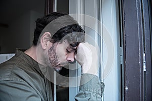 Depressed man looking out a window at home in mental health concept