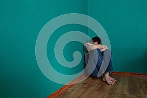 Depressed man sits in a corner in an empty green room with his head in his lap.