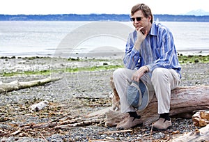 Depressed man sitting on driftwood on beach