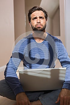 Depressed man sitting on floor using laptop