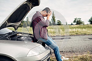 Depressed man sitting on a hood of broken car