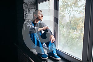 Depressed man sitting on the window sill, psycho