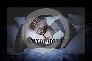 Depressed man with smartphone in bed at night. Autophobia - fear of isolation