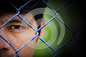 Depressed man standing behind a fence ,close up on face