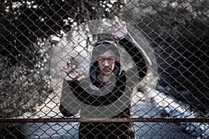 Depressed man wearing a black hoodie standing behind a fence han