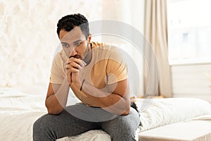 Depressed Middle Eastern Man Sitting Thinking In Modern Bedroom