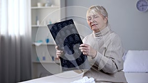 Depressed old lady looking at brain x-ray and crying, incurable disease, health photo