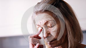 Depressed old lonely woman wiping tears with tissue while looking through the window