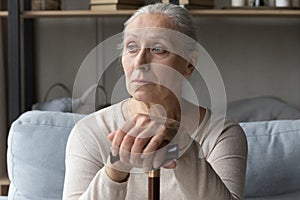 Depressed old woman sitting on couch, leaning on cane