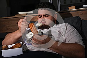 Depressed overweight man eating sweets in room at night photo