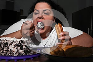 Depressed overweight woman eating sweets in kitchen