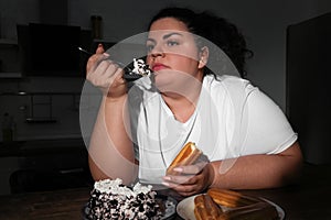 Depressed overweight woman eating sweets in kitchen