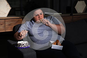 Depressed overweight woman eating sweets in room at night