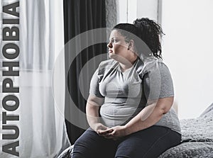 Depressed overweight woman sitting alone on bed. Autophobia
