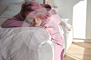 Depressed pensive teen girl introvert pink hair lying on bed looking away.