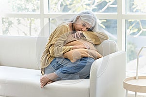 Depressed retired elderly woman sitting on couch at home