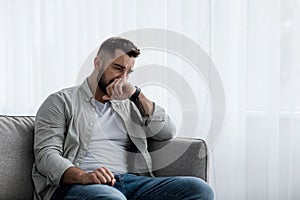 Depressed sad attractive man crying on sofa at home, feeling lonely, tired and worried