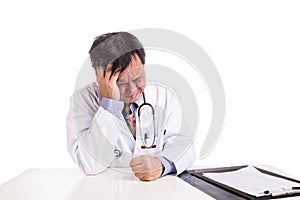 Depressed sad matured Asian doctor seated behind desk