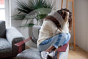 Depressed sad woman holding head in hands sitting on armchair