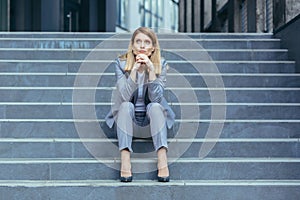 Depressed sad woman sitting on the stairs of a business building, businesswoman in business clothes tired