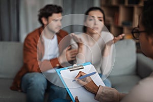 Depressed sad young european husband calm, support wife talking to psychologist in clinic interior