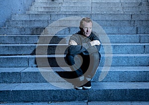 Depressed sad young man crying sitting on stairs feeling miserable lonely in urban scene