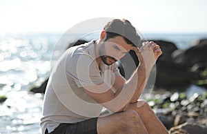 Depressed sad young man sitting on a sea beach