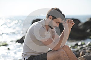 Depressed sad young man sitting on a sea beach