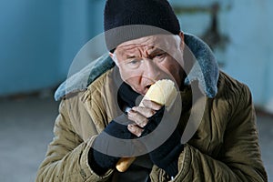 Depressed senior-aged beggar eating bread